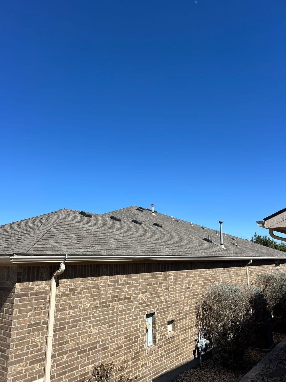 Residential roof under clear blue sky with ventilation pipes and brick walls.