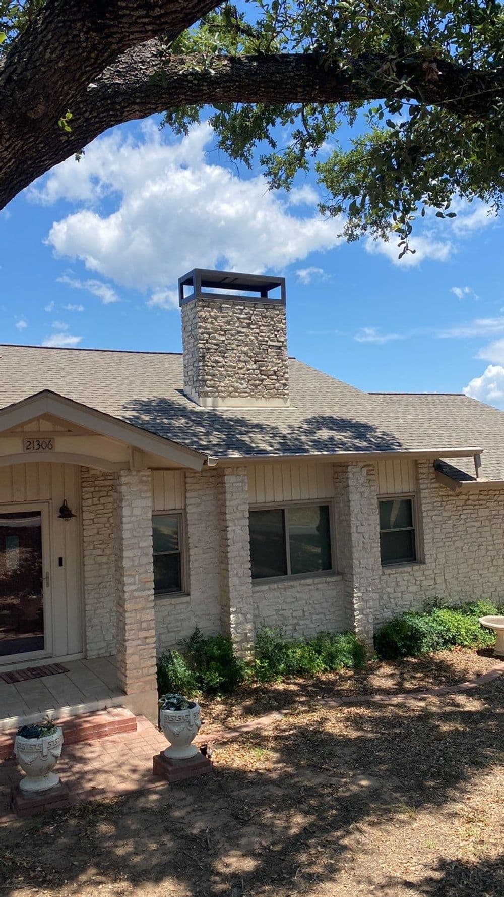 Charming home with a stone chimney, surrounded by greenery and blue skies.