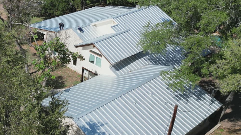 Aerial view of a house with a new metal roof installation surrounded by trees.