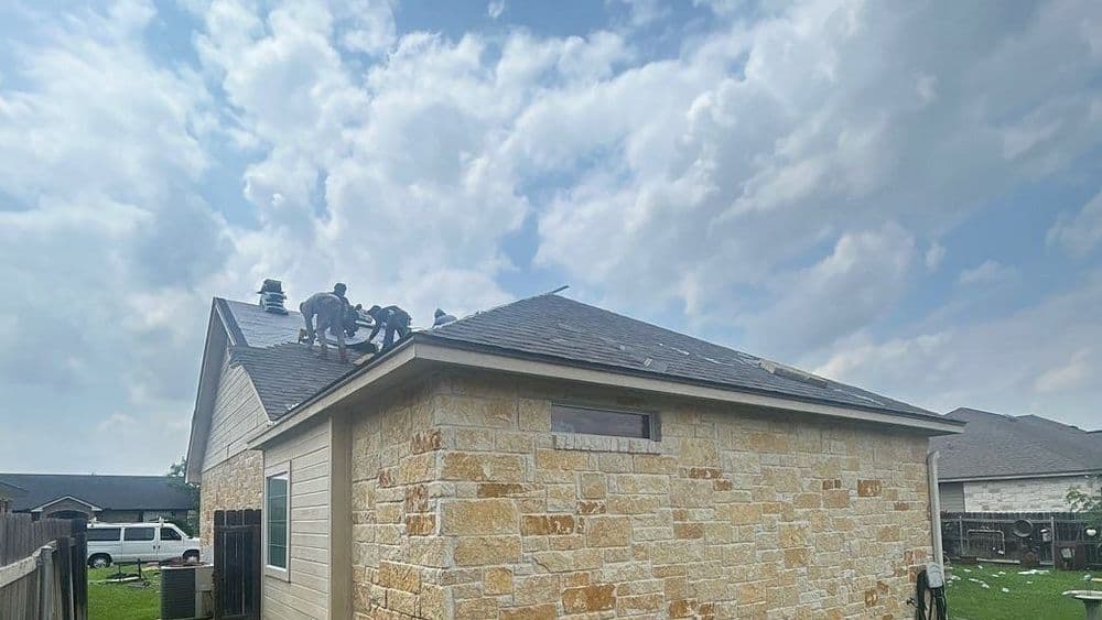 Roofing contractors working on a house with a cloudy sky in the background.