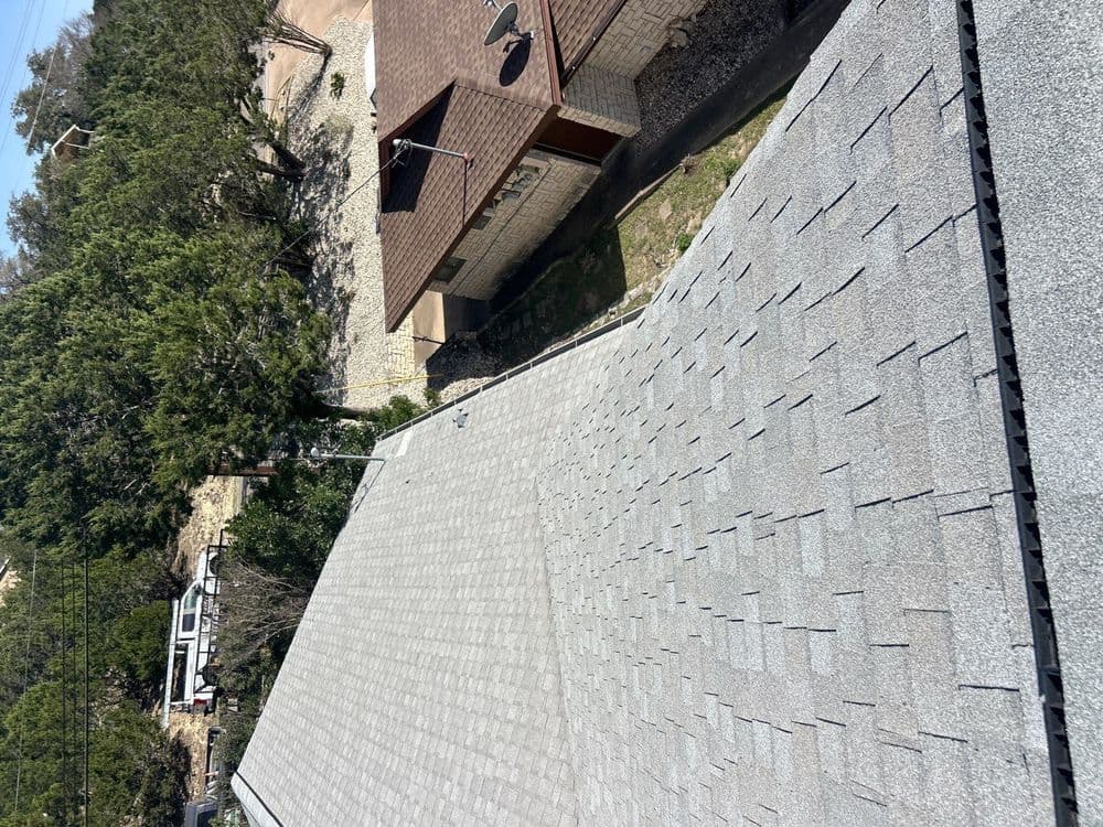 Aerial view of a gray shingle roof alongside a house and trees.