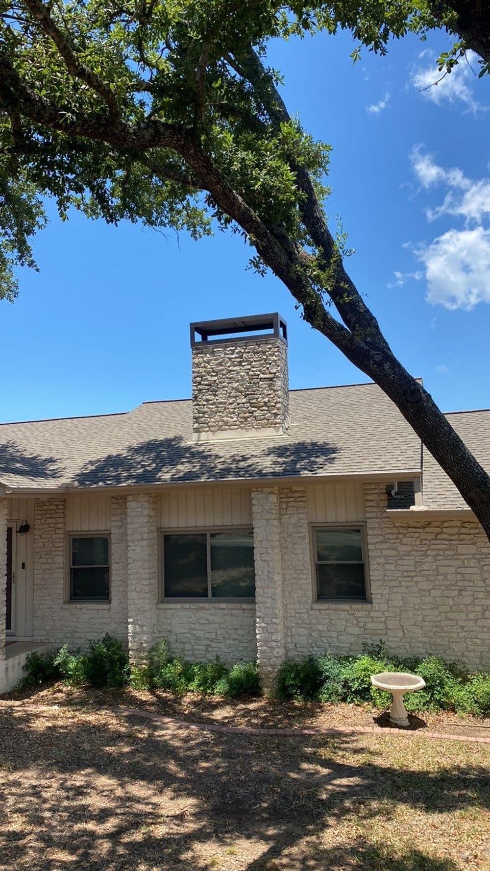 Charming stone house with chimney, surrounded by trees and blue sky. Ideal family home.