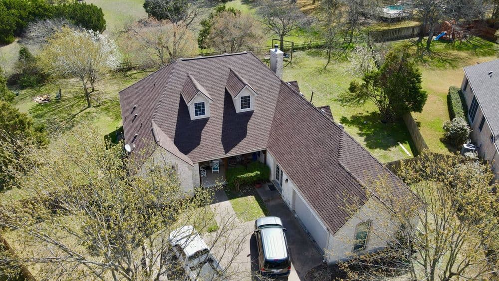 Aerial view of a suburban home with a brown roof surrounded by trees and greenery.