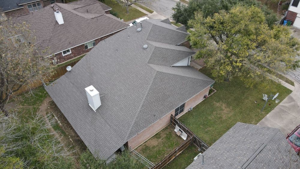 Aerial view of residential roof with gray shingles and surrounding yard, showcasing landscaping.