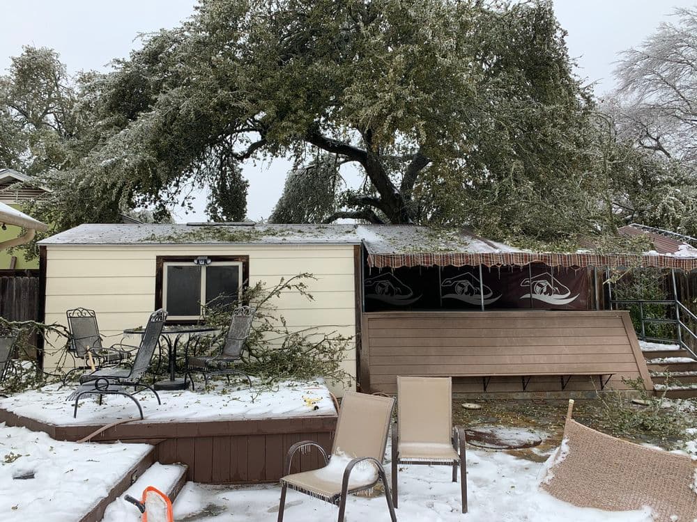 Snow-covered shed with fallen tree branches and patio furniture in a winter landscape.