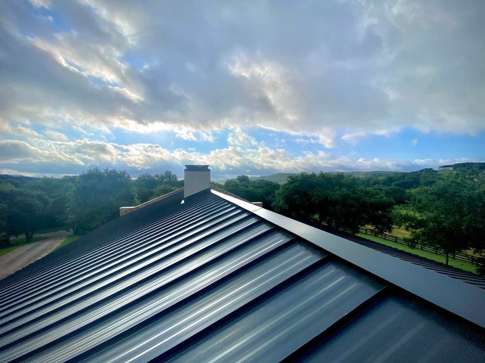 View of a metallic roof with clouds and green landscape in the background.