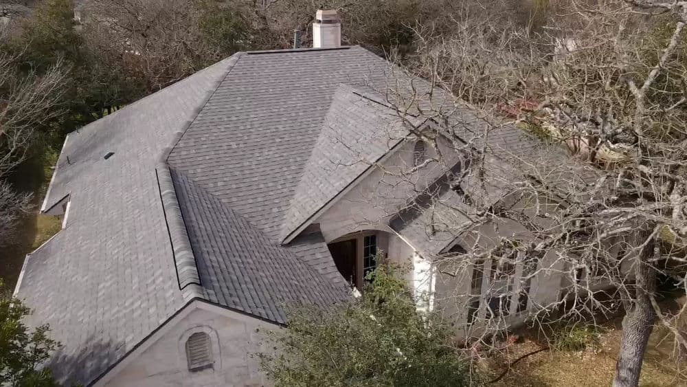 Aerial view of a residential home with a gray shingle roof and surrounding trees.