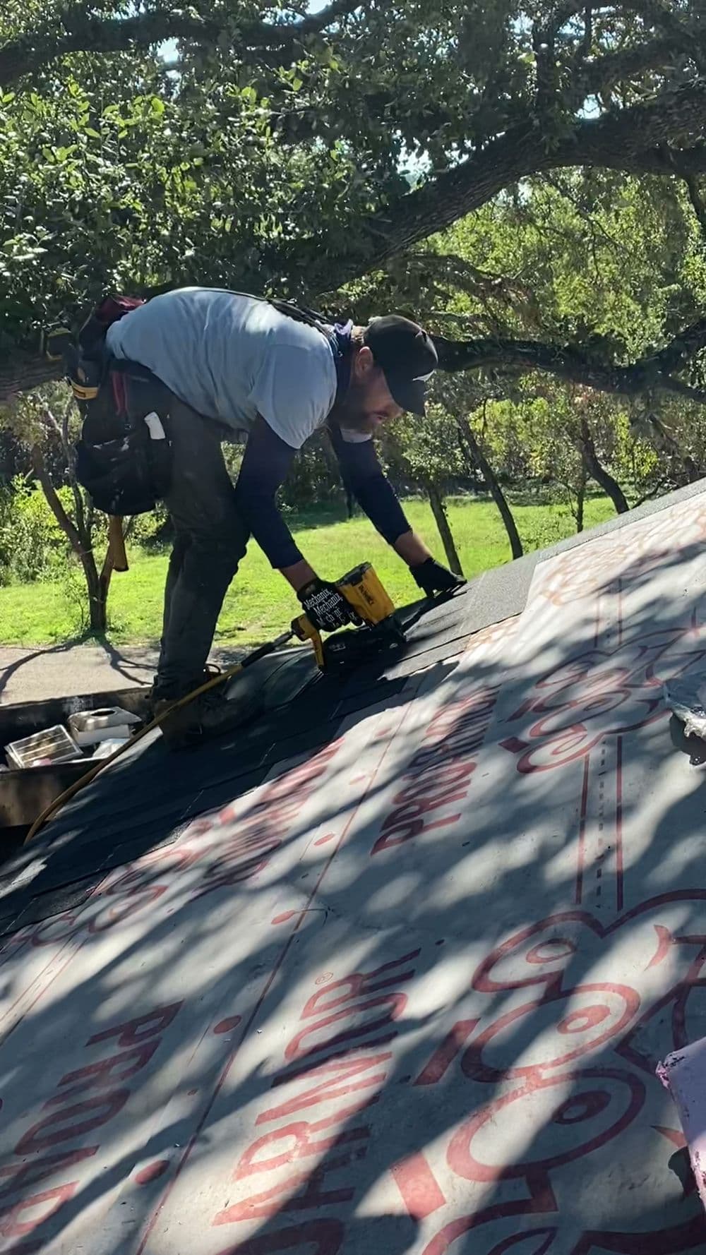 Roofer installing shingles on a residential roof under sunny conditions.