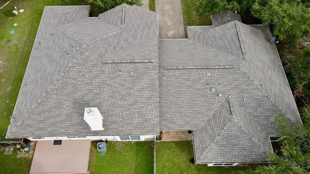 Aerial view of a residential roof with gray shingles and surrounding green lawn.