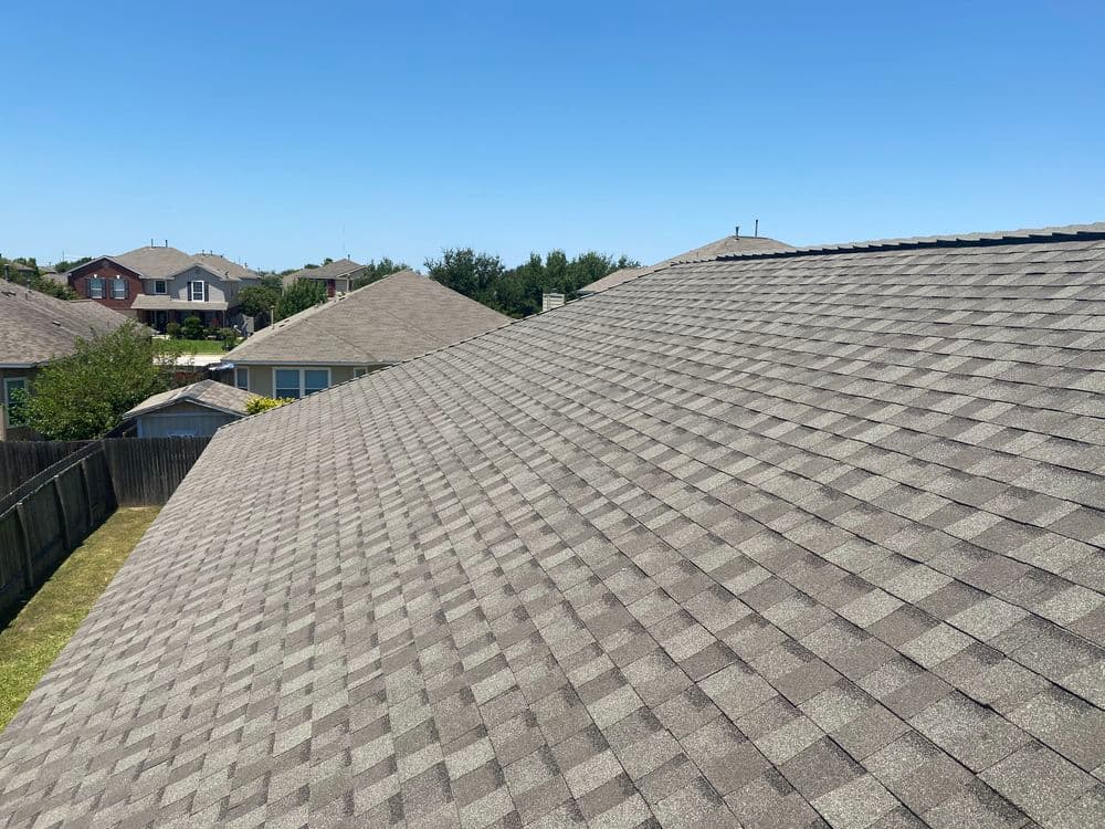 Overview of residential neighborhood roofs under a clear blue sky with shingles.