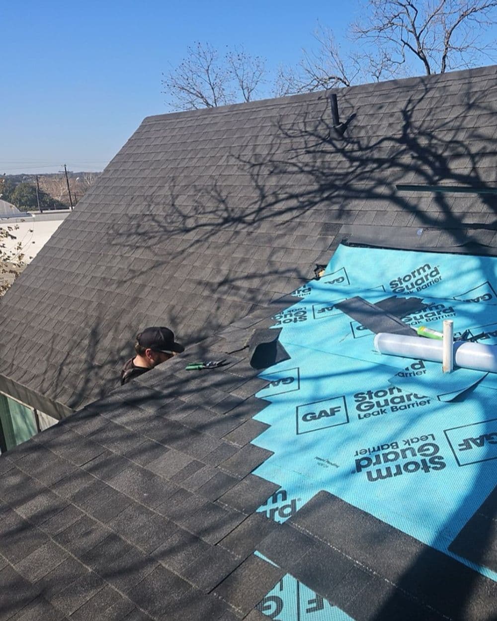 Roofer installing StormGuard Lock Barrier on a residential roof under blue sky.