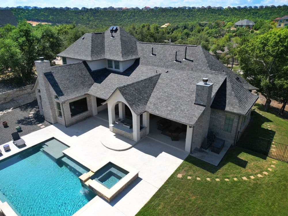 Aerial view of modern luxury home with pool and patio in a lush green landscape.