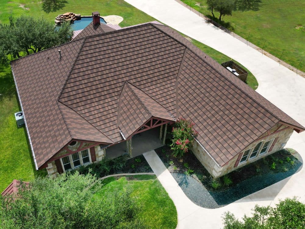 Aerial view of a house with brown tiled roof and landscaped yard, featuring a pathway and greenery.