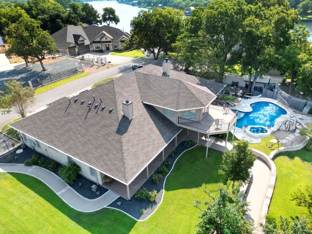 Aerial view of a modern home with a pool, lush lawn, and scenic surroundings.